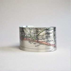 May include: A silver metal cuff bracelet featuring a vintage map of Brighton, England printed on it. The map shows the names of streets and landmarks, including Patcham, Falmer, and Black Rock.