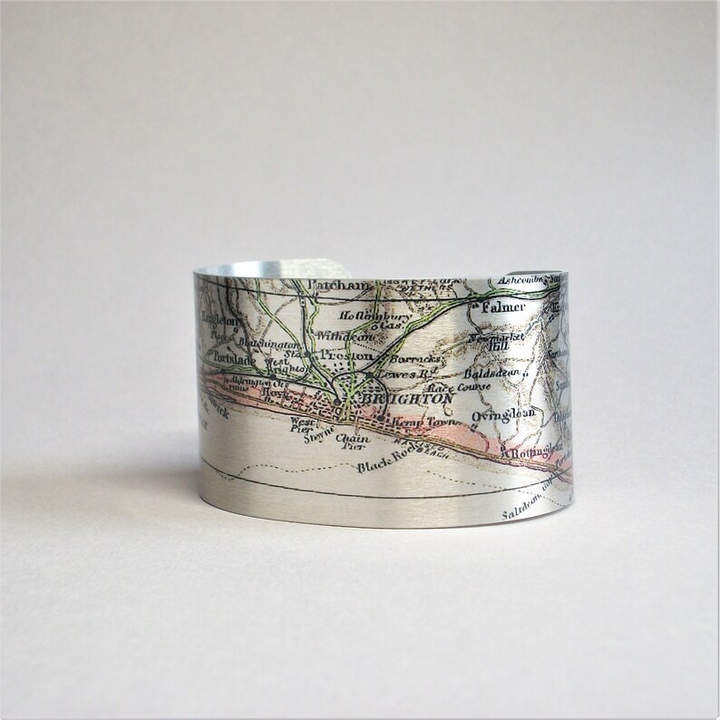 May include: A silver metal cuff bracelet featuring a vintage map of Brighton, England printed on it. The map shows the names of streets and landmarks, including Patcham, Falmer, and Black Rock.