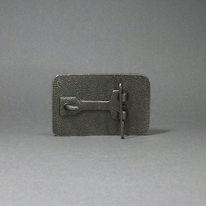 May include: A silver metal belt buckle with a textured surface and a hook and loop closure.