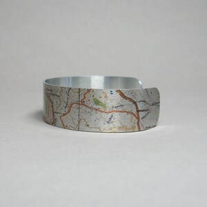 May include: A silver metal bracelet with a map design. The map features a variety of geographical features, including roads, rivers, and towns. The bracelet is a unique and stylish way to show your love for travel and adventure.