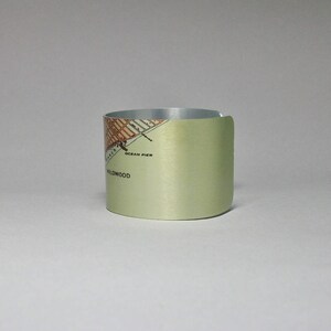May include: A light green metal beverage coaster with a map of Wildwood, New Jersey printed on it. The map includes the text "Ocean Pier" and "Wildwood".