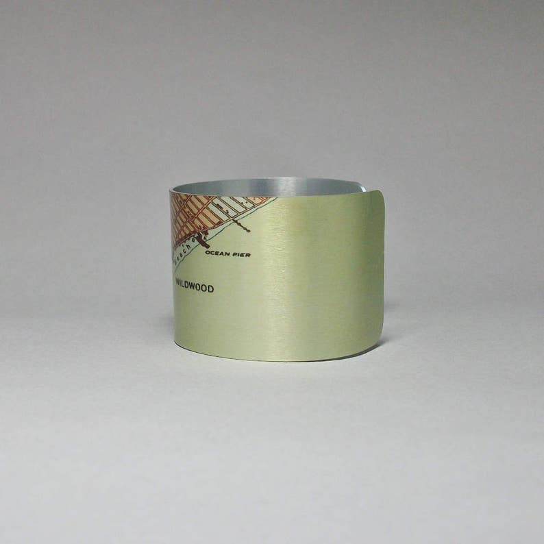May include: A light green metal beverage coaster with a map of Wildwood, New Jersey printed on it. The map includes the text "Ocean Pier" and "Wildwood".