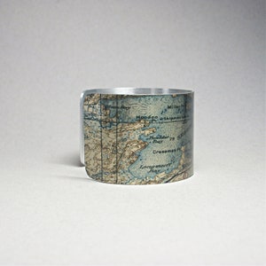 May include: A silver-toned cuff bracelet with a vintage map design. The map features blue and tan tones, with geographical details. The bracelet is a wide band, showcasing the map's intricate details. A unique accessory.