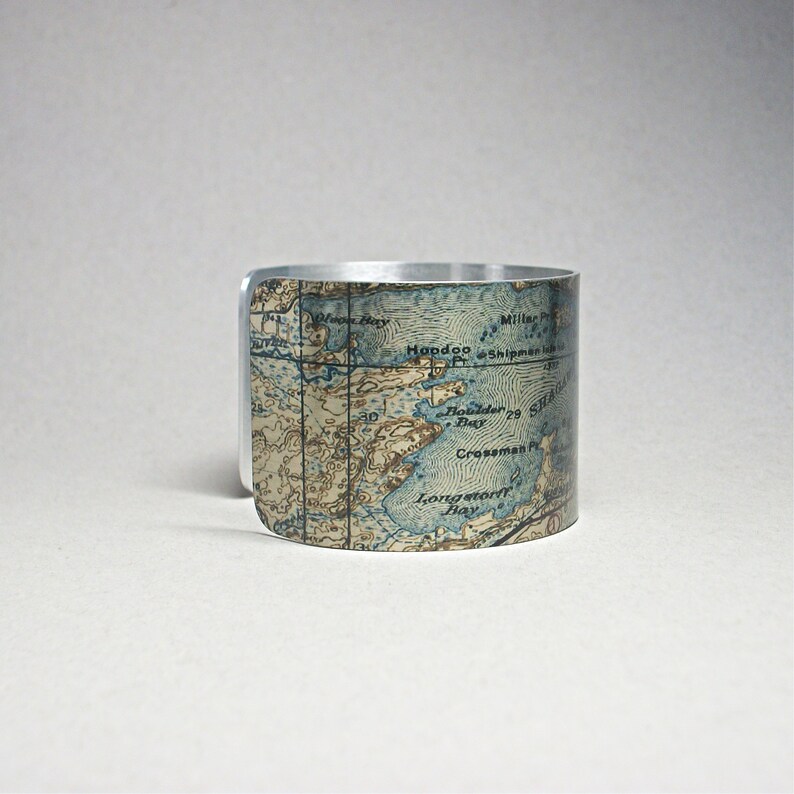 May include: A silver-toned cuff bracelet with a vintage map design. The map features blue and tan tones, with geographical details. The bracelet is a wide band, showcasing the map's intricate details. A unique accessory.