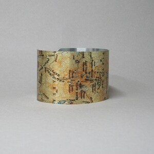 Puede incluir: Un brazalete de metal plateado con un dise&ntilde;o de mapa vintage que incluye el texto "South Sister", "Lane Co", "Deschutes Co", "Lost Creek Glacier", "Fronty Glacier" y "Three Sisters".