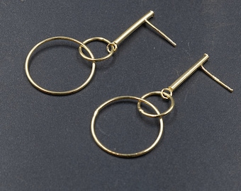 Könnte beinhalten: Ein Paar goldfarbene Ohrringe mit einem langen, dünnen Stab und zwei verbundenen Kreisen. Die Kreise sind unterschiedlich groß, wobei der größere Kreis unter dem kleineren Kreis hängt.