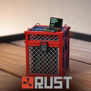 May include: A red cage with a silver wire mesh front and a small laptop on top. The laptop screen displays a green interface with the number 1457. The word "RUST" is displayed in a white font at the bottom of the image.