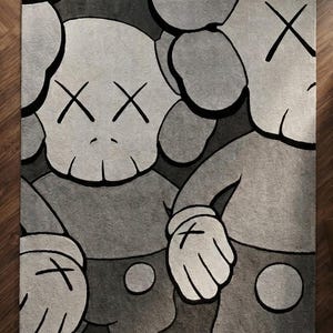 K&ouml;nnte beinhalten: Ein rechteckiger Teppich mit einer grafischen Illustration von zwei Zeichentrickfiguren mit totenkopfartigen K&ouml;pfen, X-f&ouml;rmigen Augen und behandschuhten H&auml;nden. Das Design ist in Grau-, Schwarz- und Wei&szlig;t&ouml;nen mit kr&auml;ftigen schwarzen Konturen gehalten.