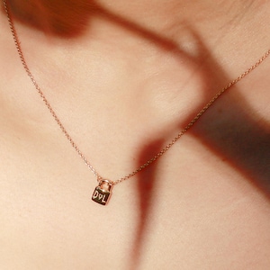 May include: A fine rose gold necklace with a tiny padlock pendant. The pendant is inscribed with the initials "D&L". The necklace is worn around a person's neck, highlighting its refined aesthetic.