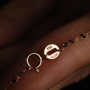 Pu&ograve; includere: Primo piano di una chiusura e di una catena di collana in oro. La chiusura &egrave; un piccolo anello a molla rotondo. La catena &egrave; delicata con un motivo a maglie ovali ripetute. La chiusura ha i marchi "FSS" e "Au585".