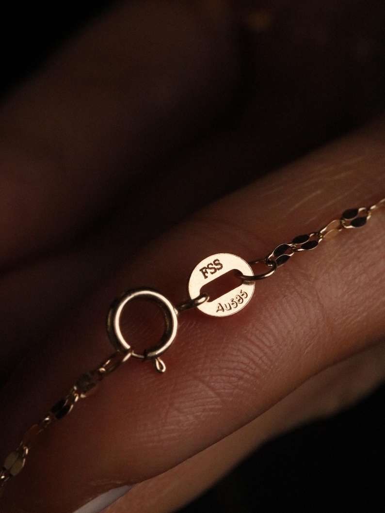 Pu&ograve; includere: Primo piano di una chiusura e di una catena di collana in oro. La chiusura &egrave; un piccolo anello a molla rotondo. La catena &egrave; delicata con un motivo a maglie ovali ripetute. La chiusura ha i marchi "FSS" e "Au585".