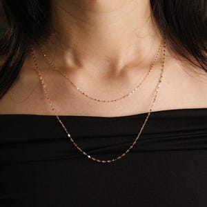 Pu&ograve; includere: Una collana dorata a pi&ugrave; strati con maglie delicate. La collana &egrave; mostrata su uno sfondo nero, evidenziando la lucentezza del gioiello. Le catene hanno una sottile brillantezza, aggiungendo un tocco di eleganza al design. Un accessorio semplice ma elegante.