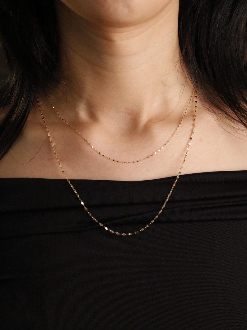 Pu&ograve; includere: Una collana dorata a pi&ugrave; strati con maglie delicate. La collana &egrave; mostrata su uno sfondo nero, evidenziando la lucentezza del gioiello. Le catene hanno una sottile brillantezza, aggiungendo un tocco di eleganza al design. Un accessorio semplice ma elegante.