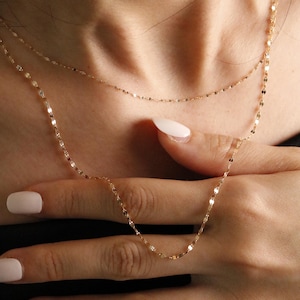 Delicate 14k solid gold necklace featuring tiny faceted links, resting on skin and fingers to highlight its fine texture and dainty scale