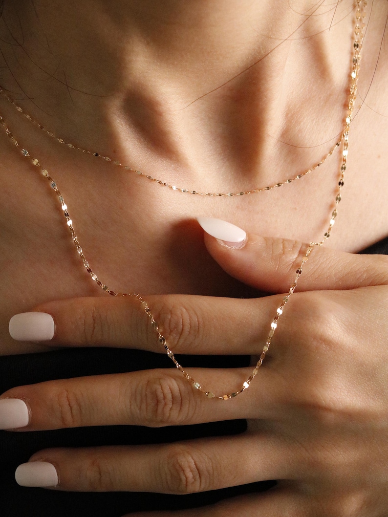 Delicate 14k solid gold necklace featuring tiny faceted links, resting on skin and fingers to highlight its fine texture and dainty scale