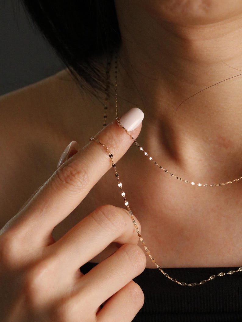 Minimal 14k solid gold chain with shimmering links, displayed on the neck and fingers for a clear view of its thin, lightweight proportions