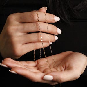 Thin 14k solid gold chain, lightly held in both hands to show its fine craftsmanship, subtle sparkle, and graceful drape, one chain width is slightly thicker 1.72mm, the second chain more dainty 1.05mm thick