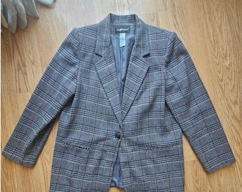May include: A gray plaid blazer with a single-button closure. The blazer features a classic notched lapel, two front pockets, and a dark gray lining. The pattern is a mix of gray, black, and tan, creating a timeless look.
