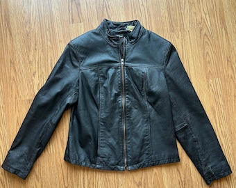 May include: Black leather jacket with a stand-up collar and a full-length zipper. The jacket has long sleeves and a tailored fit. The leather appears to be slightly distressed, giving it a vintage look. The jacket is laid flat on a wooden surface.