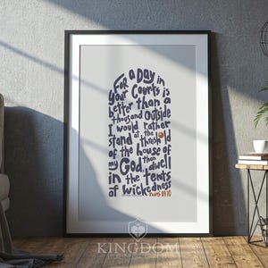 May include: Framed print with a white border, featuring a navy blue script. The text reads "For a day in your Courts is better than a thousand Outside..." with "Psalms 84:10" at the bottom. The frame is black, and the print is displayed on a wooden floor.