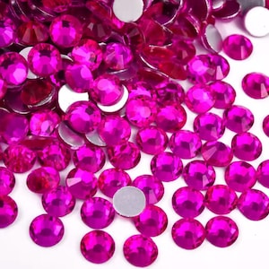 May include: A collection of vibrant fuchsia-colored rhinestones with a flat, silver backing. The faceted gems are scattered, showcasing their brilliant, reflective surfaces. These decorative embellishments are ideal for crafts and adding sparkle.