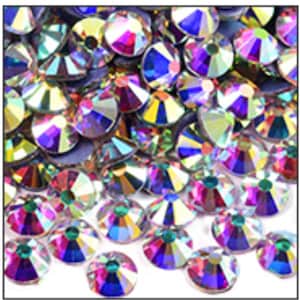 May include: A close-up of a pile of iridescent rhinestones. The rhinestones are round with a flat back and a faceted top, reflecting a rainbow of colors including purple, blue, green, and yellow. The gems are scattered, creating a sparkling effect.