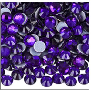 May include: A close-up view of a pile of purple rhinestones. The rhinestones are round with a faceted top and a flat, silver-colored back. The color is a deep, rich purple, and they are densely packed together.