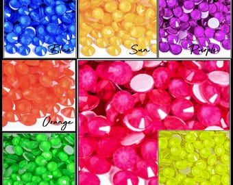 May include: A collection of colorful, faceted rhinestones in various shades. The image displays rhinestones in blue, yellow, purple, orange, pink, green, and yellow-green. Each color is labeled with a handwritten script font.
