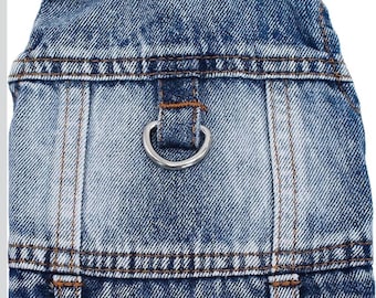 May include: A blue denim jacket featuring a folded collar, visible brown stitching, and a silver-toned metal D-ring attached to the center back panel. The garment has a classic acid-wash texture with vertical seams and a structured hemline.