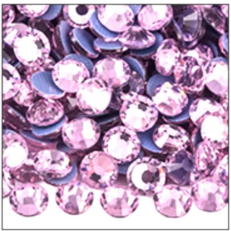 May include: Close-up of a collection of light pink rhinestones with a flat, gray backing. The rhinestones are round and faceted, reflecting light. The image shows a variety of sizes and angles of the rhinestones, creating a sparkling effect.