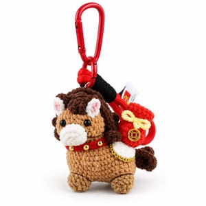 May include: A crocheted brown horse keyring featuring a dark brown mane, a white muzzle, and a red collar with gold studs. The horse carries a red sack with a yellow drawstring and a gold coin emblem, attached to a red metal carabiner clip.
