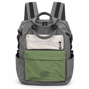 May include: A gray backpack featuring a top handle, two shoulder straps, and side pockets. The front includes a white zippered pocket above a larger green pocket with a rectangular patch displaying the text "MAZEVO & BAG" at the bottom center.