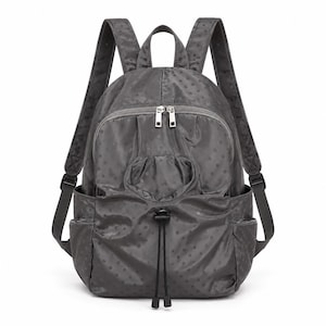 May include: A dark grey backpack featuring a subtle tonal polka dot pattern. The bag includes a top handle, two adjustable shoulder straps, a zipped front compartment, two side pockets, and a central drawstring closure with black toggles.