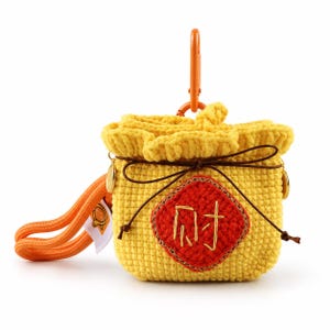 May include: A yellow crocheted pouch with a drawstring closure, featuring a red diamond-shaped patch with the gold embroidered Chinese character for wealth. The pouch includes an orange carabiner clip and a matching orange wrist strap.