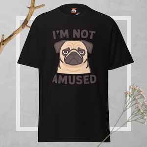 May include: Black t-shirt featuring a cartoon pug with a sad expression. The text "I'M NOT AMUSED" is above and below the pug's face. The shirt has a crew neck and short sleeves.