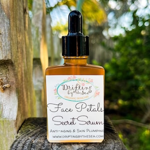 K&ouml;nnte beinhalten: Eine Glasflasche mit Gesichts-Serum und Tropfer. Die Flasche ist mit "Drifting by the Sea Organic Skincare Face Petals Secret Serum Anti-Aging & Skin Plumping WWW.DRIFTINGBYTHESEA.COM" beschriftet.