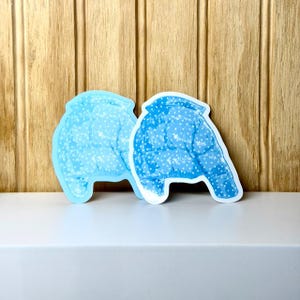May include: Two die-cut stickers featuring a bright blue puffer jacket design with a white polka dot pattern. The stickers are shaped like the silhouette of a quilted jacket with a collar and sleeves, displaying a repeating white dot motif.
