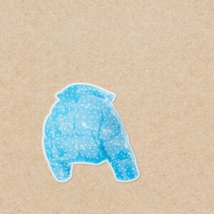 May include: A light blue puffer jacket with white polka dots. The jacket is shown from the back, with a white outline. The background is a light brown, textured surface.