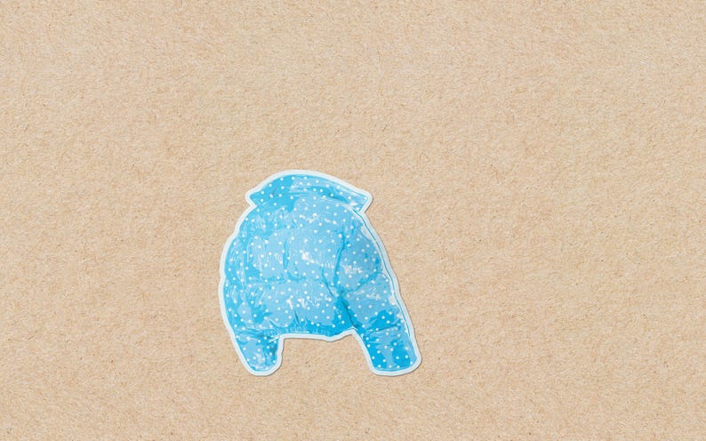 May include: A light blue puffer jacket with white polka dots. The jacket is shown from the back, with a white outline. The background is a light brown, textured surface.