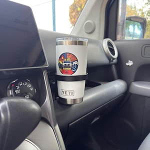 May include: A white stainless steel tumbler with a clear lid, featuring a circular graphic sticker that depicts a vehicle and the text IN MY ELEMENT. The tumbler has a YETI logo printed near the base and is held in a black cup holder mount.