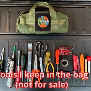 May include: An olive green tool bag with a patch, surrounded by various tools. The tools include screwdrivers, pliers, scissors, and a multi-tool. The text "Tools I keep in the bag (not for sale)" is displayed.