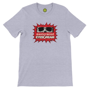 May include: Light gray t-shirt with a graphic featuring a skull wearing sunglasses inside a red burst. The text "mastermind EYESCREAM" is below the graphic. A small smiley face logo is on the upper back.