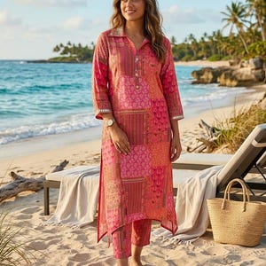 Puede incluir: Conjunto de túnica y pantalón patchwork rosa y coral. La túnica tiene cuello y cierre de botones. El conjunto se lleva en una playa de arena, con un bolso de mano de paja en el fondo.