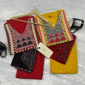 Puede incluir: Dos conjuntos a juego, uno rojo y otro amarillo, cada uno con una parte superior estampada y pantalones lisos. Las partes superiores tienen diseños intrincados alrededor del escote. También hay una taza negra con "Dream BIG" y otra con "Joy".