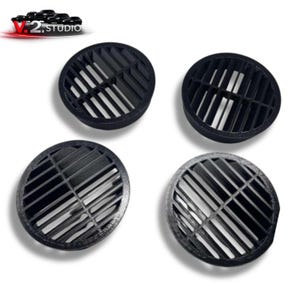 Puede incluir: Cuatro cubiertas negras y circulares para rejillas de ventilación con un diseño ranurado se muestran sobre un fondo blanco. Las rejillas tienen un patrón de rejilla, con listones angulados que crean una estética geométrica. El logotipo "V.2. Studio" es visible en la esquina superior izquierda.