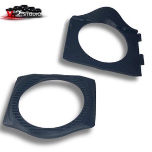 May include: Two dark blue, angular plastic components with oval openings. The parts have a textured surface and appear to be designed for a specific mechanical or electronic application. The V.2 Studio logo is in the upper left corner.