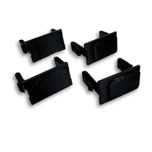 Puede incluir: Cuatro clips rectangulares de plástico negro con una superficie texturizada. Cada clip tiene una pequeña pestaña rectangular que se extiende desde un lado. Los clips están dispuestos sobre un fondo blanco.