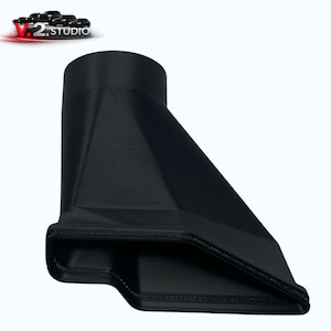 May include: A black, 3D-printed nozzle with a rectangular opening and a cylindrical top. The nozzle has a geometric design with angled sides and a smooth, matte finish. The V.2 Studio logo is in the top left corner.
