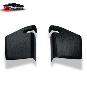 May include: Two black plastic car seat belt guides. Each guide has a textured surface and a curved top with a hole. The guides are designed to help position seat belts for optimal safety and comfort.
