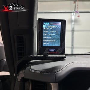 Könnte beinhalten: Ein schwarzes digitales Anzeigegerät, das auf einem Armaturenbrett montiert ist. Der Bildschirm zeigt verschiedene Motorleistungswerte an, darunter Ladedruck, Motorlast und Temperatur. Das Ford Performance-Logo ist sichtbar.